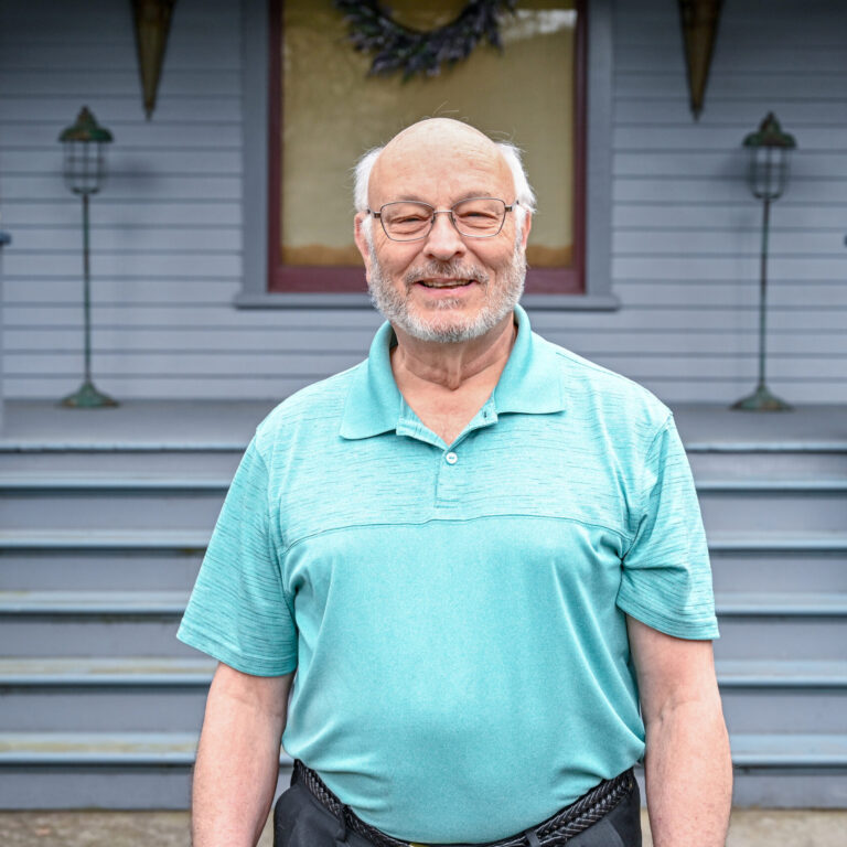 Man smiling and standing in front of blue house